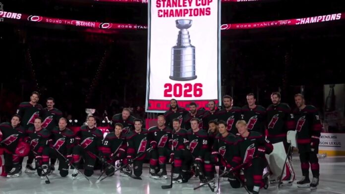 Hurricanes Stanley Cup banner raising 2026 Carolina Hurricanes pose for a team photo under their 2026 Stanley Cup champions banner at Lenovo Center before the season opener against the Florida Panthers