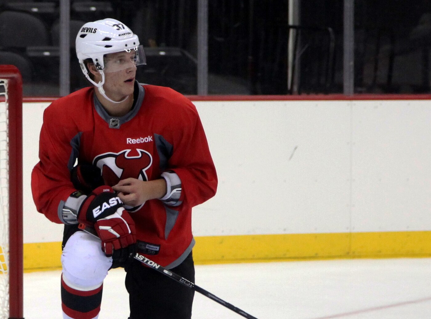Pavel Zacha kneels on the ice in a red New Jersey Devils practice jersey