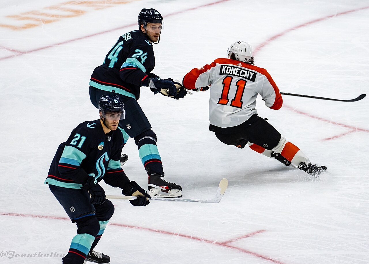 Travis Konecny drives between two Seattle Kraken defenders in a December 2023 game