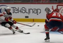 Jack Hughes Devils shoots backhand as Tom Wilson Capitals closes in during Devils-Capitals game