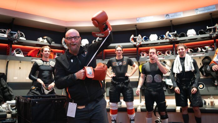 Jason Myrtetus Flyers Rocky gloves October 2026 Jason Myrtetus Flyers radio broadcaster holding Rocky gloves in locker room